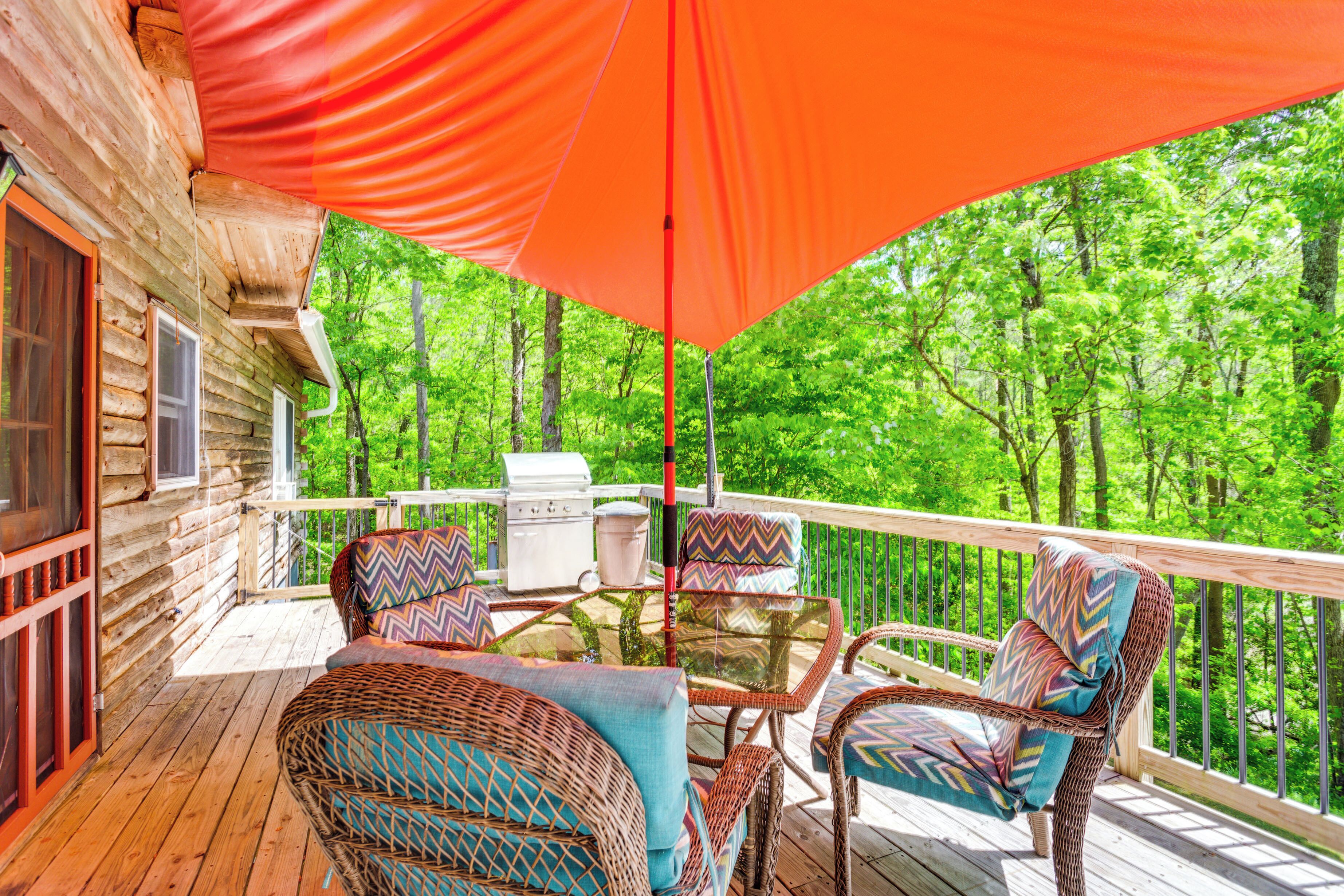 A wooden deck with wicker furniture and a grill, overlooking a forest.