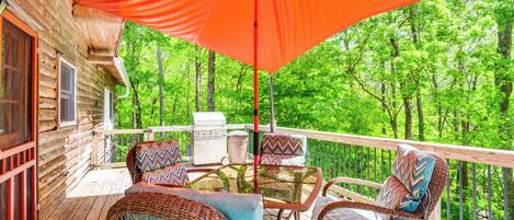 A wooden deck with wicker furniture and a grill, overlooking a forest.