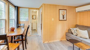 Un espacio de sala acogedor con piso de madera, un sofá, una mesa de centro y una mesa de comedor con sillas. Hay un cuadro en la pared y un equipo de aire acondicionado montado en la pared.