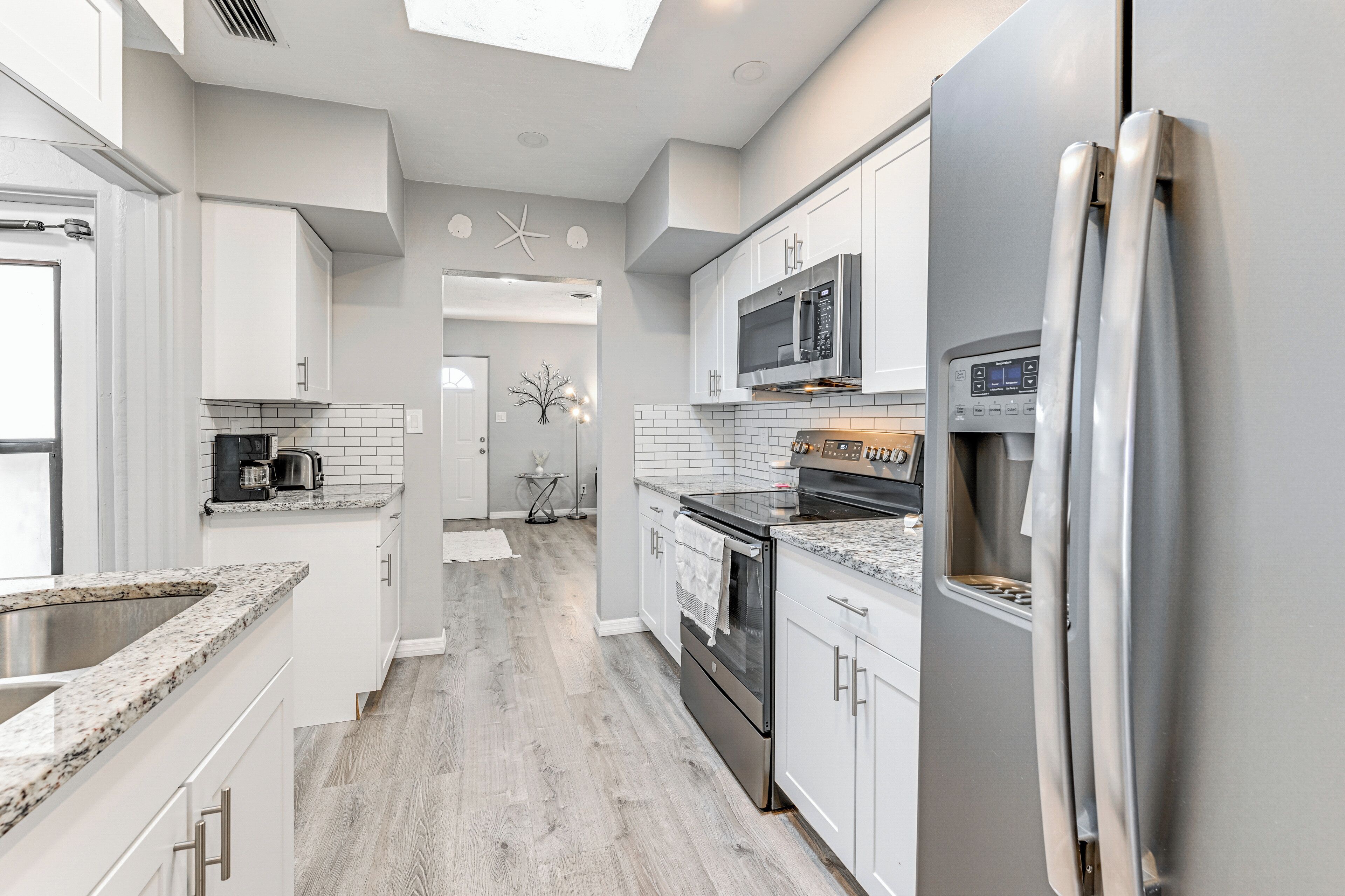 A modern kitchen with white cabinets, a stainless steel refrigerator, a microwave, and a built-in oven.