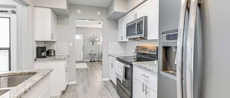 A modern kitchen with white cabinets, a stainless steel refrigerator, a microwave, and a built-in oven.
