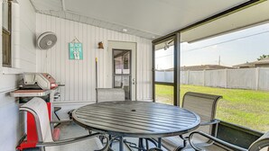 Un patio cubierto con una mesa redonda de metal y sillas de metal, un ventilador y un letrero que dice 'Beach House'.