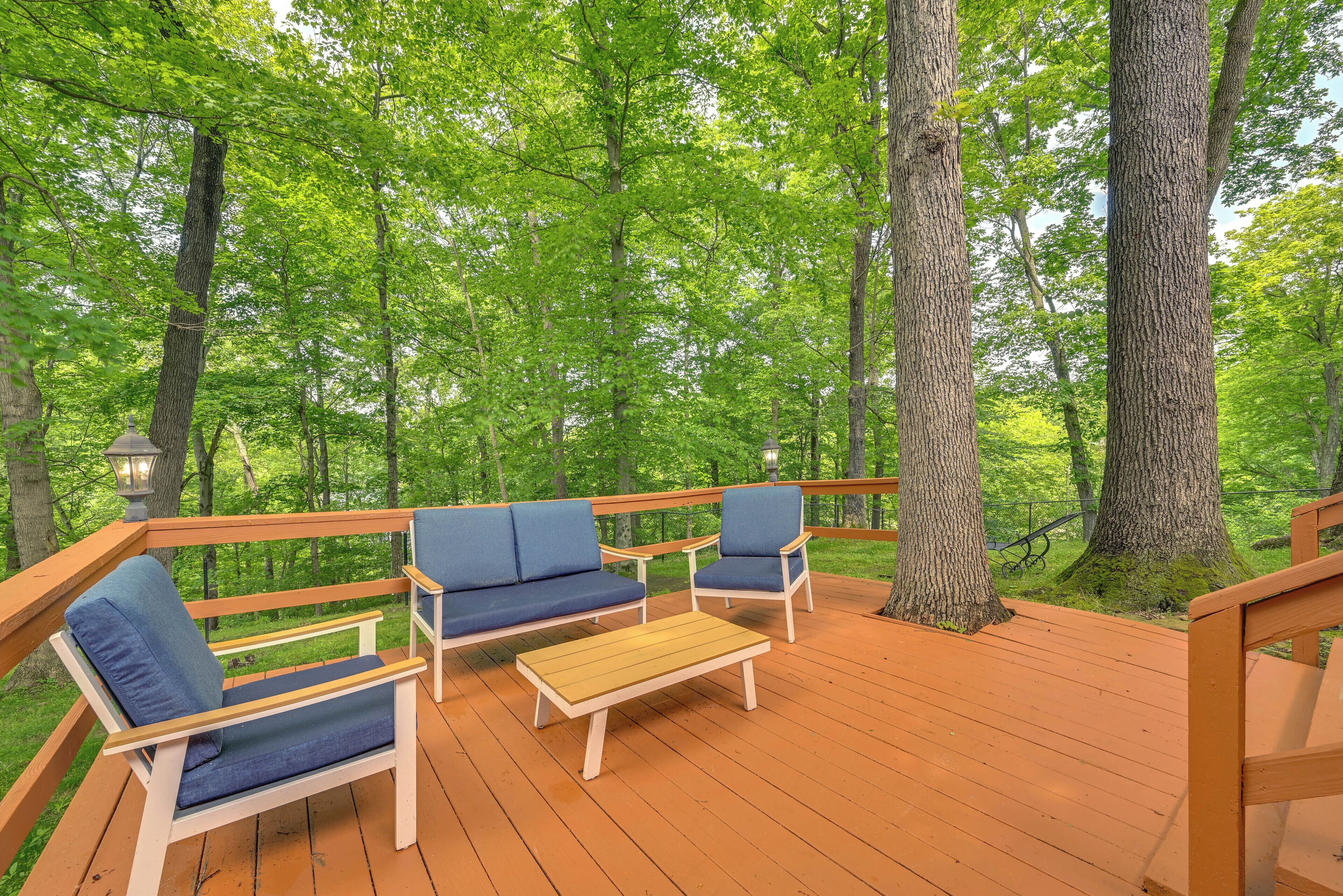 A wooden deck with blue cushioned seating and a wooden table, surrounded by trees.
