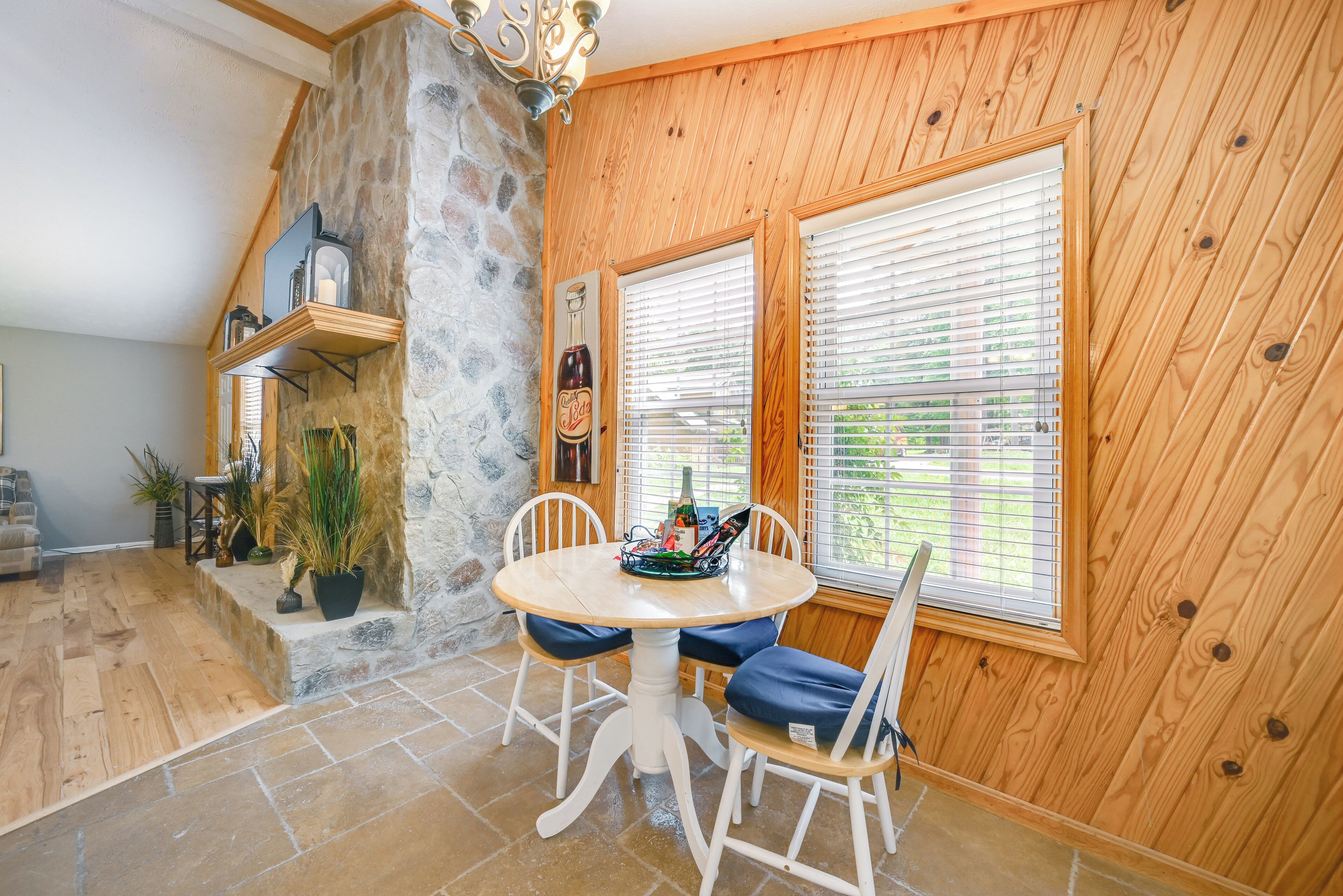 A dining area with a stone wall, wooden paneled walls, a round wooden table with blue cushions, and a bottle of beer on the wall.