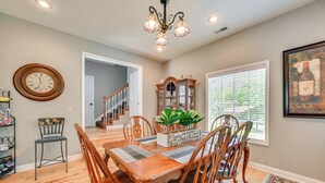 A dining area with a wooden table and chairs, a chandelier, a clock, a bookshelf, and a window with blinds. - Access to Rough River Lake! Family Home w/ Deck (Leitchfield)