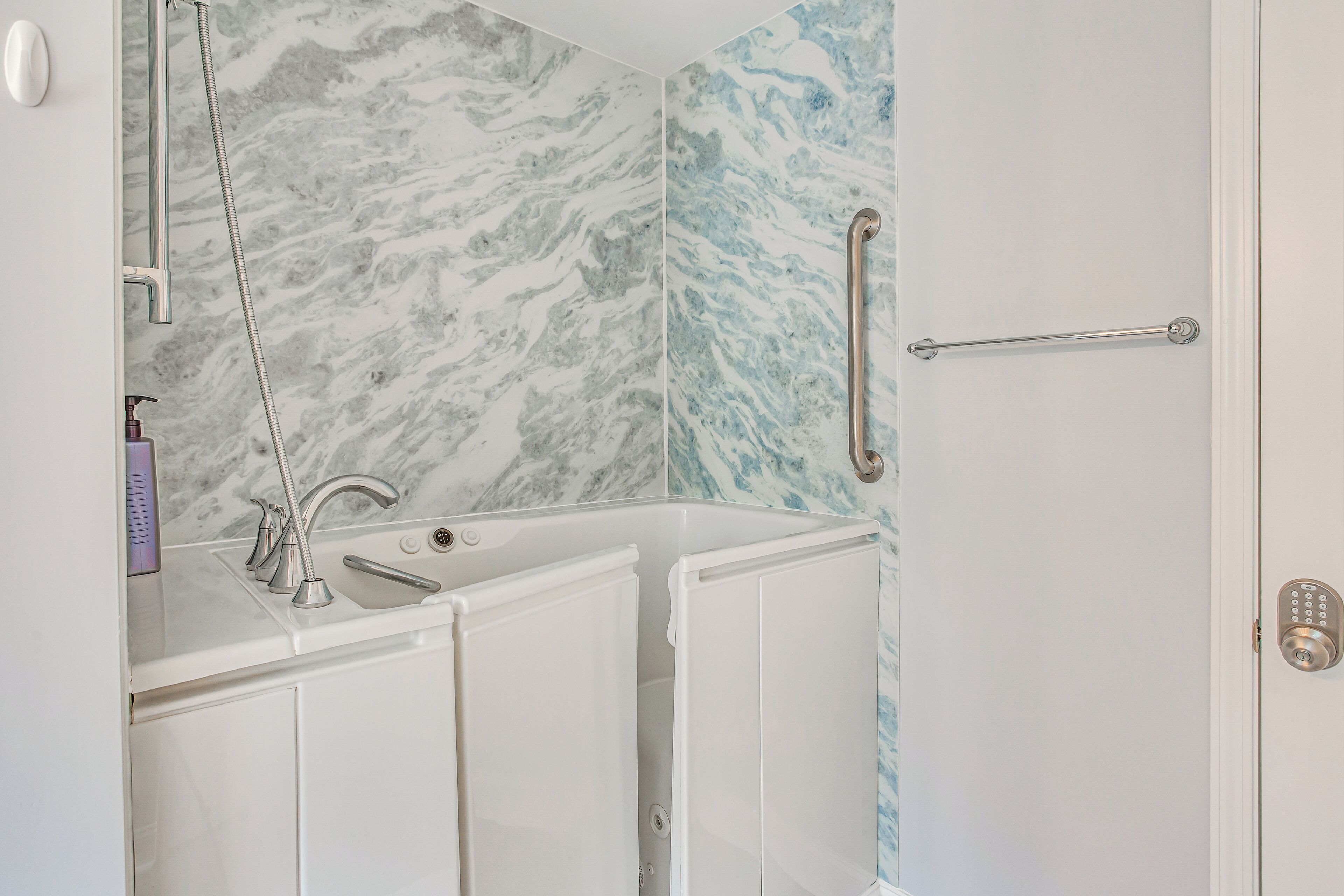 A bathroom with a marble backsplash, a bathtub, a sink with a faucet, and a door with a handle and lock.