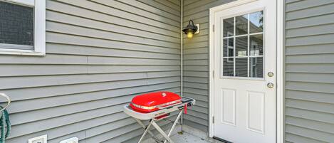 A house exterior with a red grill on a wheeled cart, a door with a window, and a welcome mat.