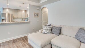 Un soggiorno moderno con un divano angolare beige, angolo cottura con elettrodomestici in acciaio inossidabile e una porta con la scritta "SALTY".