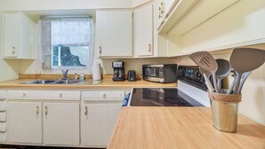 A kitchen with white cabinets, a wooden countertop, a sink, a stove, a microwave, and a coffee maker.