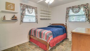 A bedroom with a bed, a ceiling fan, a dresser, and a window with curtains.