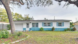 A single-story house with a garage, a front yard with a tree, and a small garden area.