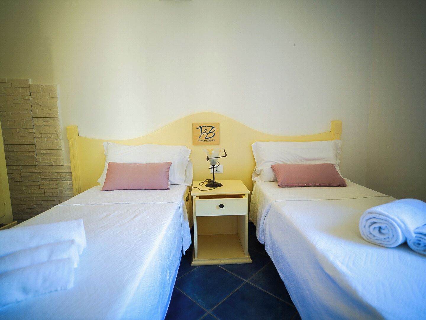 A double room with two beds, a nightstand, a lamp, and a wall-mounted sign.