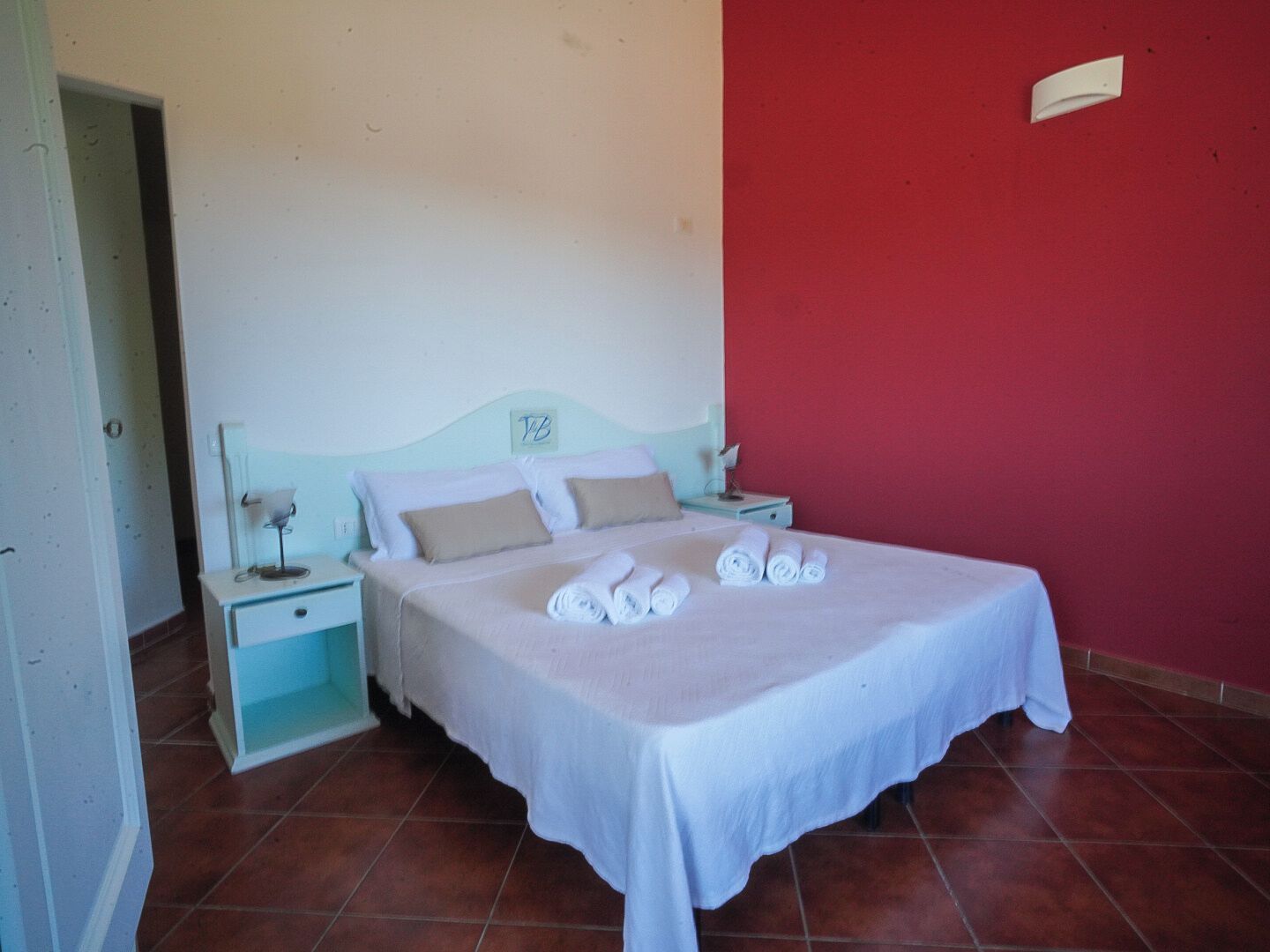 Une chambre à coucher avec un lit, deux tables de chevet, un mur rouge et une porte blanche.