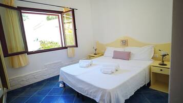 A bedroom with a bed, two bedside tables, a window with curtains, and a stone wall.