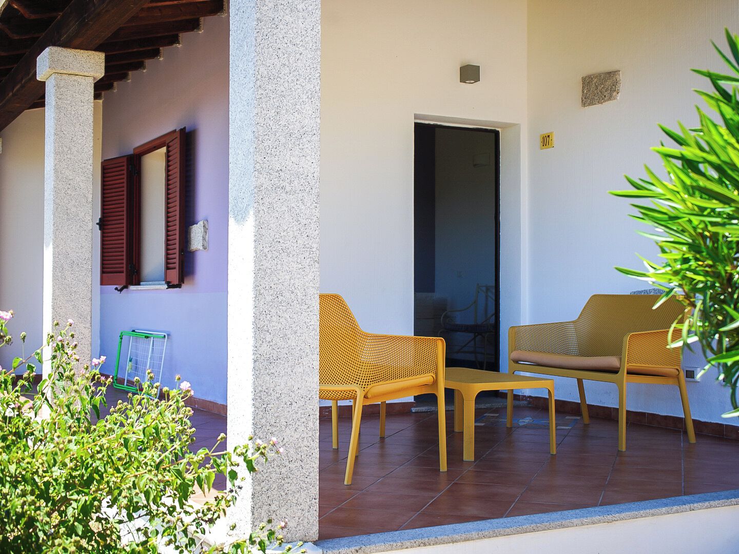 A covered outdoor seating area with wicker furniture, a door, and a potted plant.