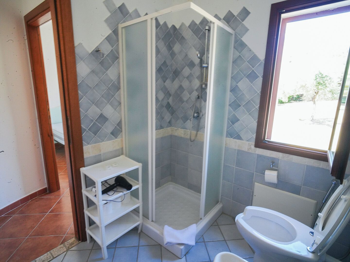 Een badkamer met een douche, toilet en een raam.