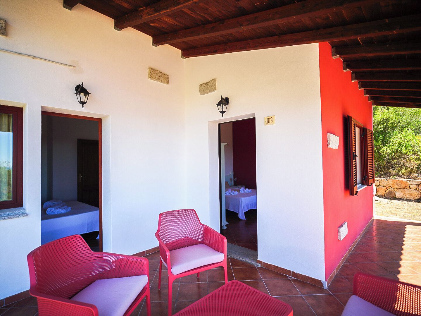 A hotel room with a red exterior, a tiled patio, and red wicker furniture.