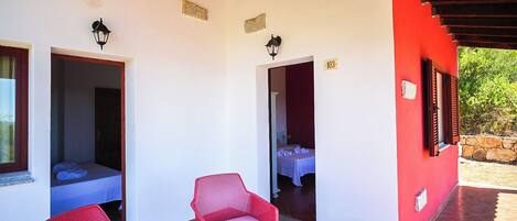 A hotel room with a red exterior, a tiled patio, and red wicker furniture.