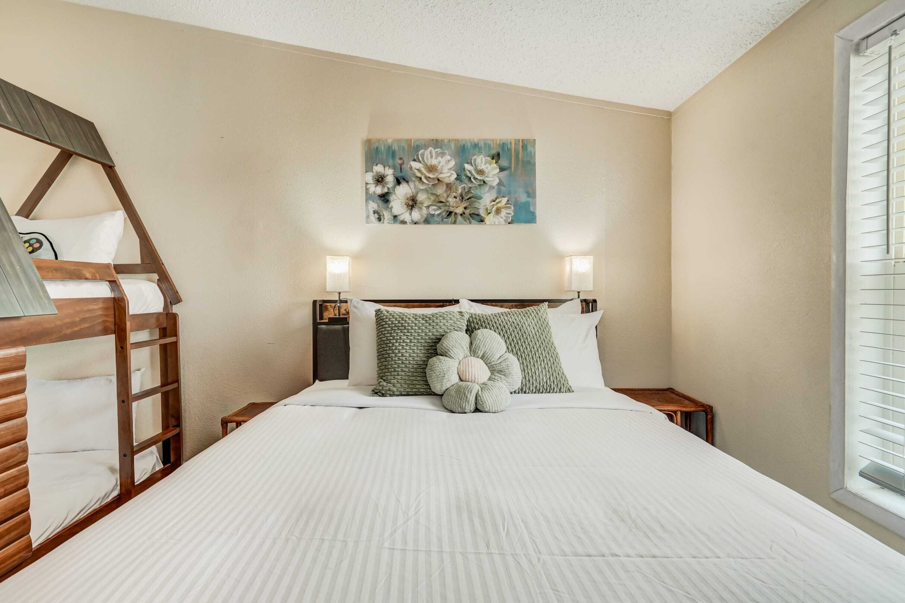 A bedroom with a bunk bed, a painting of flowers, and a window with blinds.