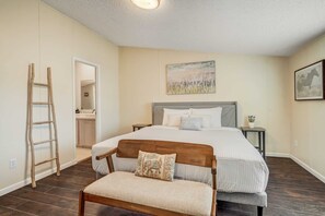 A bedroom with a bed, a nightstand, a chair, a ladder, and a bathroom visible through an open door.
