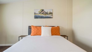A bedroom with a bed, two nightstands, a painting on the wall, and a window.