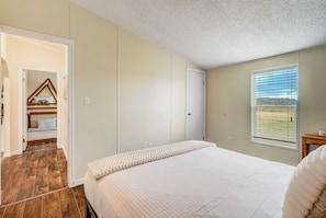 Ein Schlafzimmer mit Bett, Kleiderschrank, Fenster mit Aussicht und einer Tür zu einem anderen Raum.