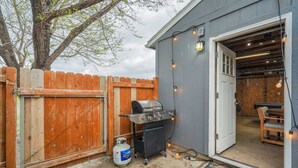 A backyard with a barbecue grill, a wooden fence, and a door leading to an interior space.