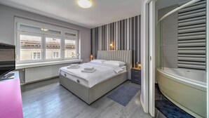 A modern bedroom with a large bed, a window with blinds, a bathtub, and a radiator. - Silver Apartment With Hot Tub And Balcony (Zagreb)