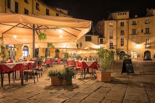 An outdoor café with tables and chairs, potted plants, and a chalkboard menu.