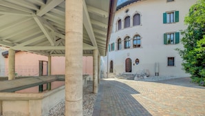 A covered outdoor area with a cobblestone path leading to a building with arched windows and a stone staircase.