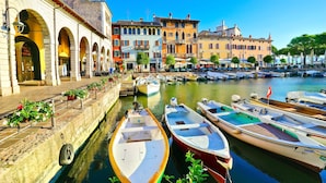 A canal with boats docked, a row of colorful buildings, and a clear blue sky.