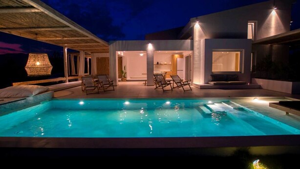 Un área de piscina moderna al aire libre, con sillones de descanso y un espacio interior bien iluminado.