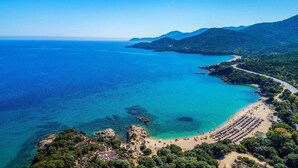 Vista aérea de una zona costera con playa, aguas azules cristalinas y una carretera que lleva a la playa.