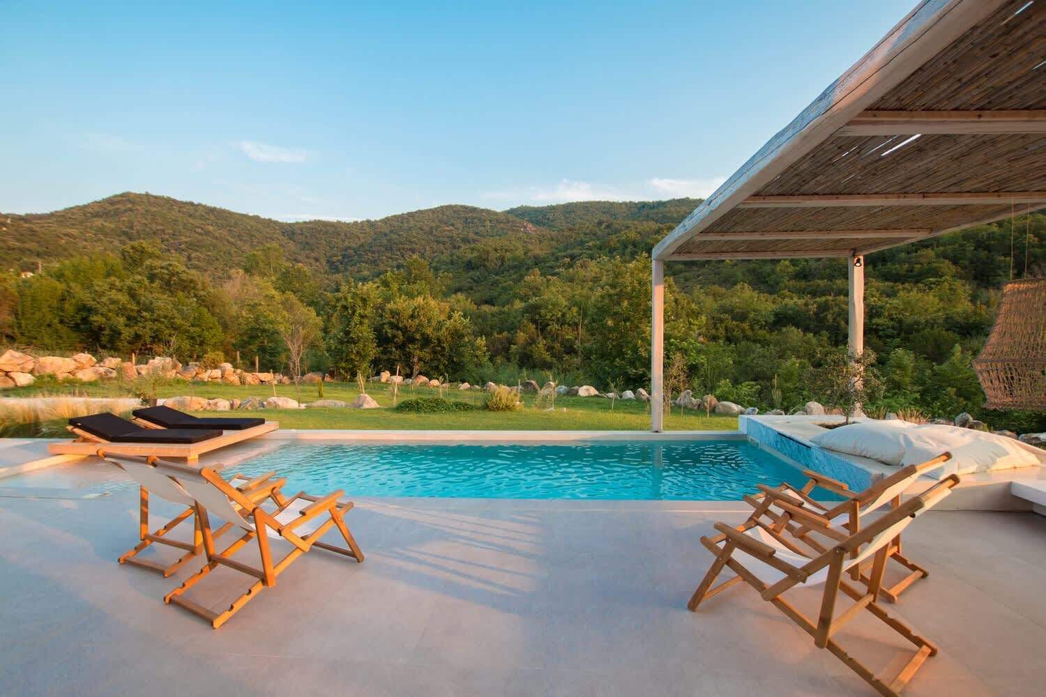 Un espace piscine doté de chaises longues en bois et offrant une vue sur un paysage montagneux.