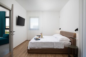 A modern hotel room with a wooden bed, a flat-screen TV mounted on the wall, a small bedside table, and a window with sheer curtains. - Villa Rudina in Pomer (Pomer)