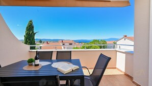 Un balcon avec une table, des chaises, une bouteille de vin et un livre ouvert.