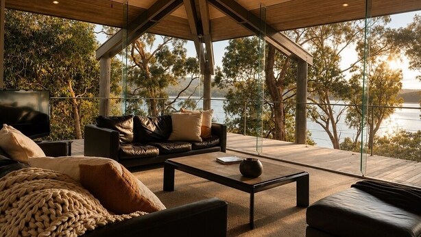 A modern living room with a large window overlooking a body of water, furnished with leather sofas and a coffee table. - Glasshouse Lake Eildon Architectural Retreat (Taylor Bay)
