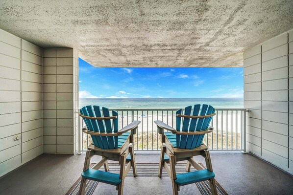 A balcony with two Adirondack chairs facing a beach view.