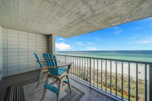 A balcony with two blue Adirondack chairs, a view of the beach, and a clear sky.