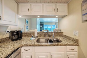 A kitchen with white cabinets, a granite countertop, a coffee maker, and a sink.