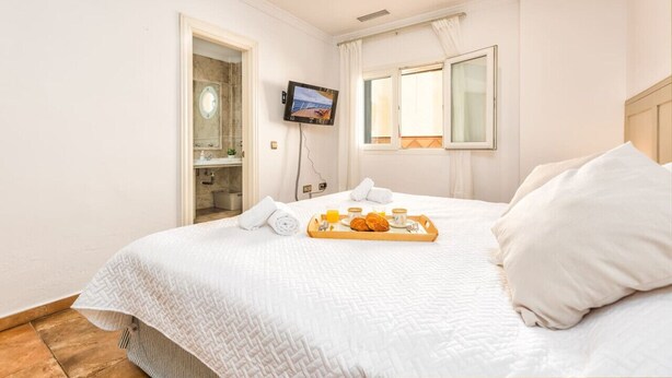 Habitació d'hotel amb un llit, un televisor fixat a la paret, una finestra amb cortines i un safata amb articles per esmorzar al llit.