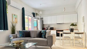 Un salon moderne avec une table basse en verre, un canapé agrémenté de coussins à motifs et une vue sur la cuisine.
