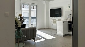 Une cuisine moderne dotée d’un téléviseur à écran plat, d’un coin repas avec un canapé et une table en verre, et offrant une vue sur le balcon extérieur.