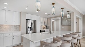 A modern kitchen with white cabinetry, a central island, bar stools, and pendant lighting.