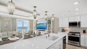 A modern kitchen with white cabinetry, a large island with a sink, stainless steel appliances, and pendant lighting.