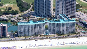 A large hotel complex with multiple high-rise buildings, a beachfront, and a golf course in the background.