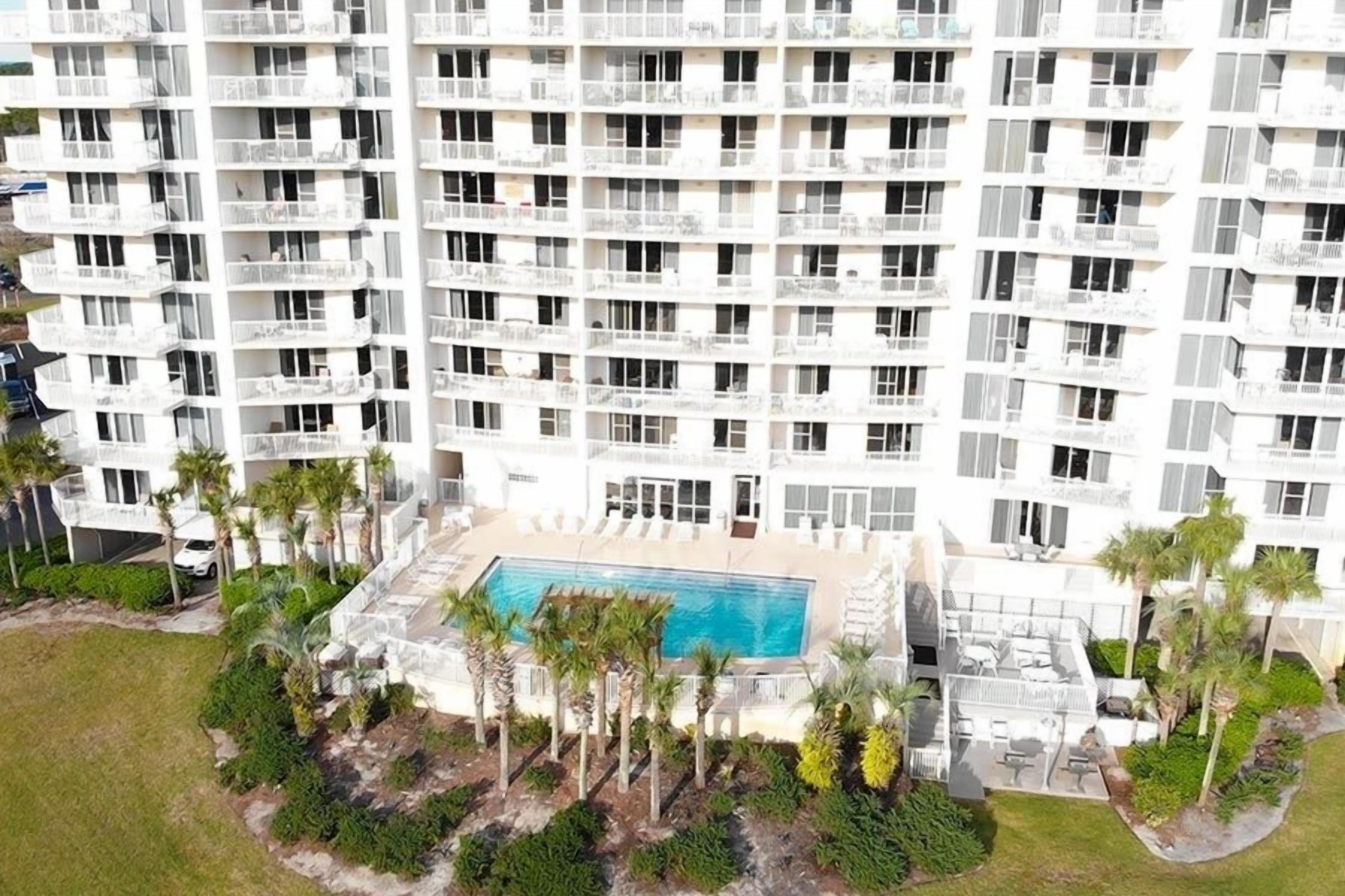 Un edificio de gran altura con múltiples balcones, una piscina y zonas verdes circundantes.