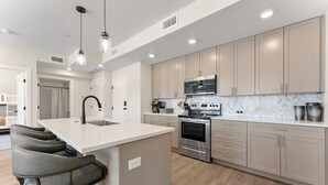 A modern kitchen with a central island, stainless steel appliances, and light wood cabinetry.