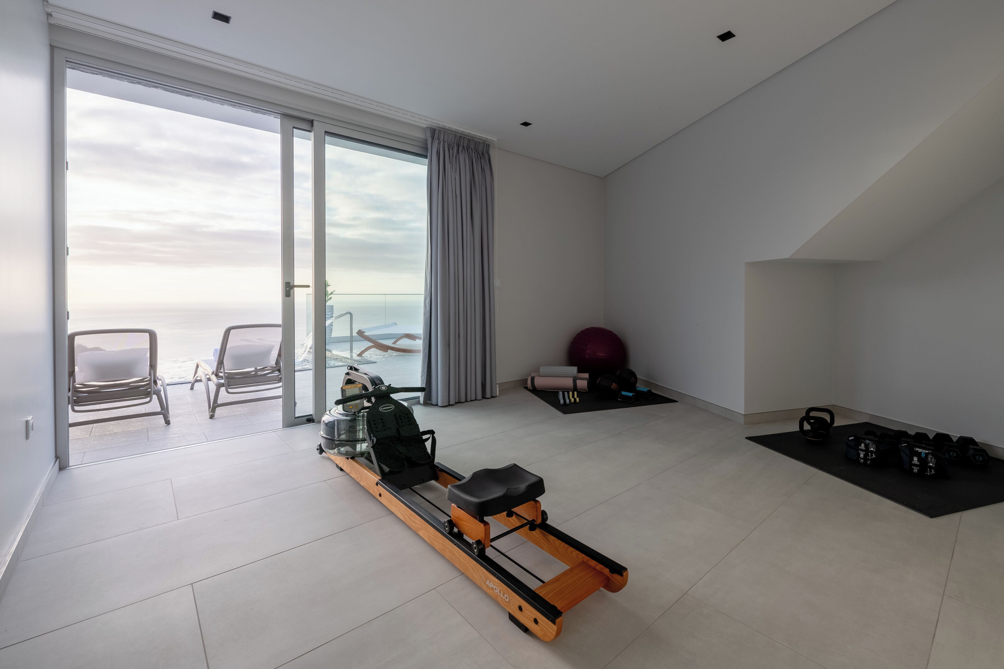 A modern living room with a rowing machine, exercise balls, and dumbbells.