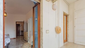 Ein Flur mit einem Bett, einem Holzschrank und einer Tür, an deren Wand ein Korb hängt.